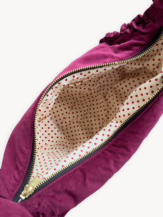 Close-up of burgundy bag 
with a gold zipper and polka dot lining on a white background