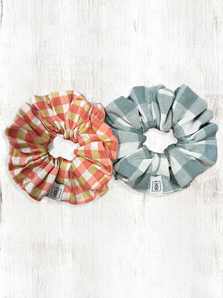 Two checkered scrunchies, one pink and yellow, one blue and white, on a light wooden surface.