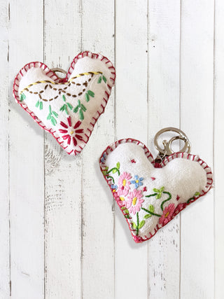 Two heart-shaped embroidered keychains on a white wooden surface