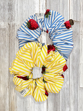Two striped scrunchies, one blue and white, one yellow and white, on a wooden surface.