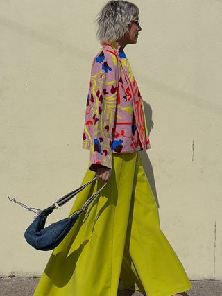 Person wearing a colorful jacket and bright yellow pants against a plain wall.