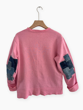 Pink sweatshirt with denim patch sleeves on a hanger against a white background