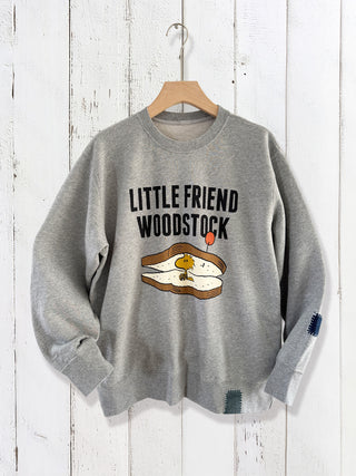 Gray sweatshirt with 'Little Friend Woodstock' text and graphic on a wooden background