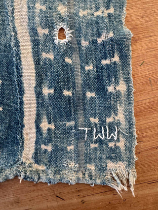Distressed denim fabric with a hole and 'TMW' branding on a wooden surface