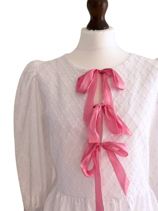 Detail of pink ribbon bows on The Bethany Top, a white broderie anglaise peplum blouse