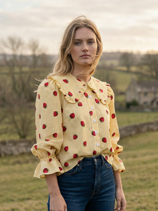 Woman wearing a yellow blouse with red polka dots and blue jeans standing in a field.