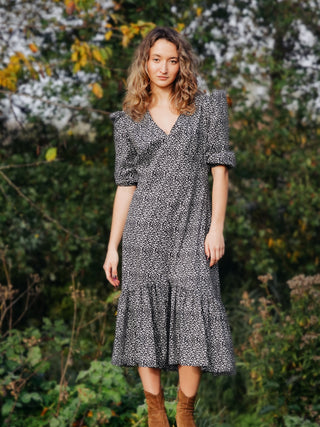 Woman wearing a black and white patterned dress standing in a natural setting.