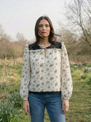 Woman wearing a floral blouse with black lace details outdoors.