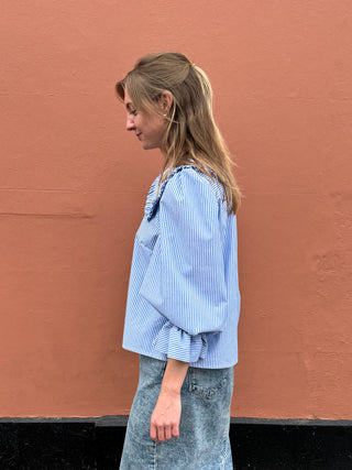 Woman wearing a blue striped blouse against a brown wall