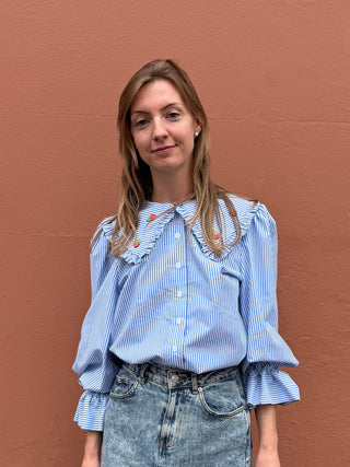 Woman wearing a blue striped shirt with ruffled sleeves against a brown wall