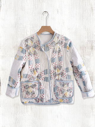 Patchwork jacket with floral patterns on a wooden hanger against a white wooden background