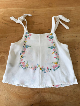 White tank top with floral embroidery on a wooden surface