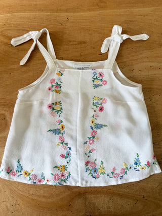 White tank top with floral embroidery on a wooden surface