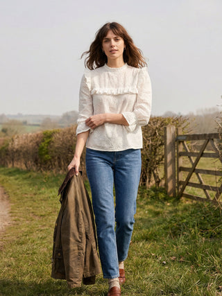 Woman in a white blouse and blue jeans holding a jacket in a field.
