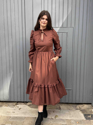 women wearing rust gingham dress stood by wall