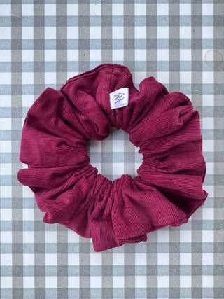 Maroon scrunchie with a brand tag on a gray and white checkered background