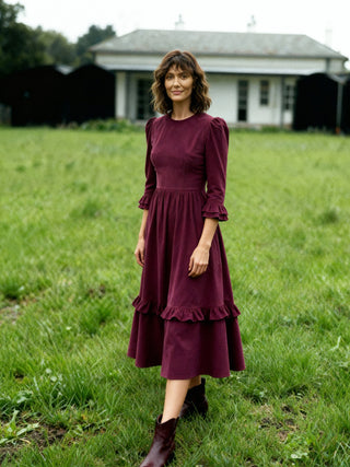 Woman in a burgundy dress standing in a grassy field with a house in the background