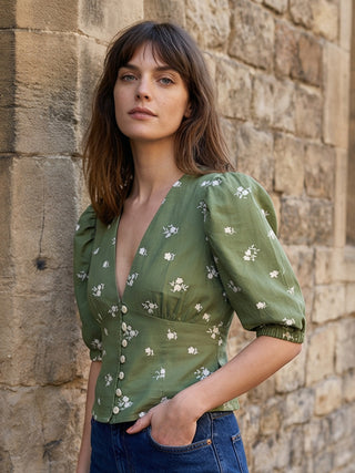 Woman wearing a green floral blouse against a stone wall