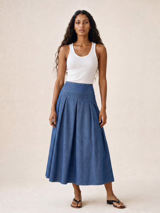 Woman wearing a white tank top and blue skirt against a beige background