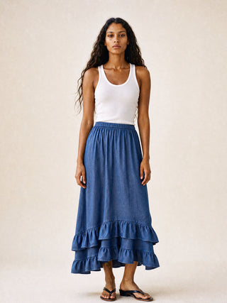 Woman wearing a white tank top and blue ruffled skirt on a plain background
