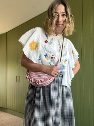 Woman wearing a white blouse with colorful embroidery and a pink bag against a green wall.