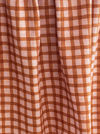 A close-up of a draped fabric with a rust-orange and light pink gingham check pattern.