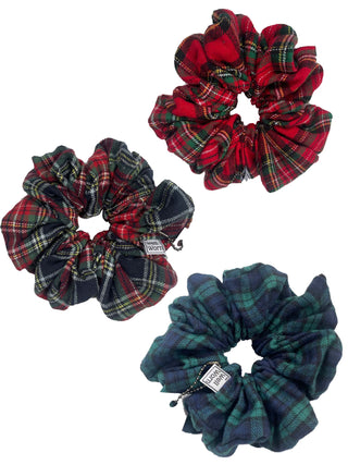 Three fabric scrunchies in tartan plaid patterns on a plain white background. One is red and green tartan, one is red and black tartan with green and yellow lines, and one is dark green and blue tartan with yellow and red lines.