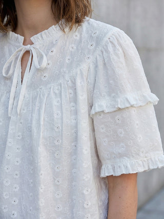 White embroidered dress with ruffled sleeves on a neutral background