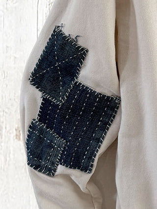 Beige garment with denim patchwork design on a white background
