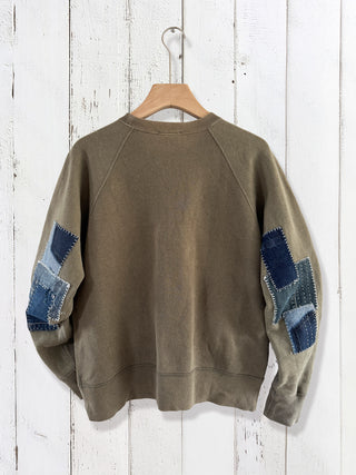 Green sweatshirt with blue patch details on a wooden hanger against a white wooden background