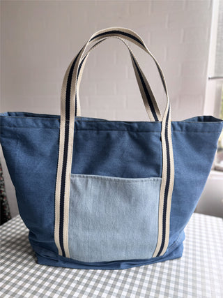 Blue tote bag with striped handles on a checkered tablecloth