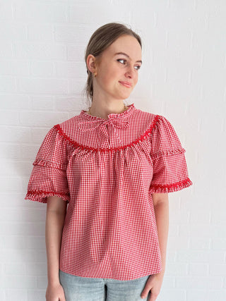 Model in the Lucy Top in red gingham, with gathered yoke and ruffle neckline, paired with denim for a chic, sustainable look