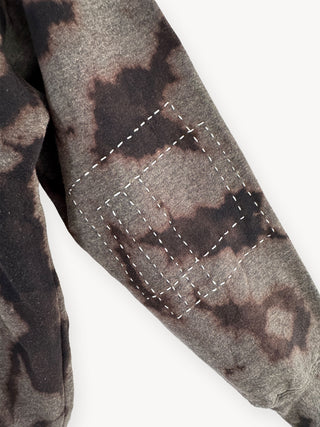Close-up of a camouflage-patterned fabric with stitching detail on a white background