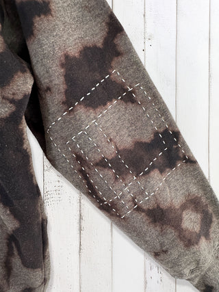 Close-up of a camouflage-patterned fabric with stitching on a wooden surface