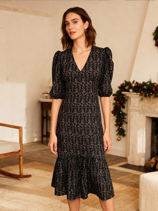 Woman wearing a black floral dress in a cozy living room.