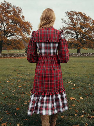 Person wearing a red plaid dress standing in a field with trees in the background