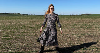 Woman in a black and white patterned dress standing in an open field with a clear blue sky.
