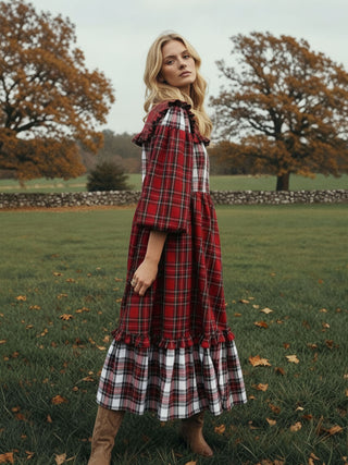Woman wearing a red plaid dress standing in an outdoor setting with trees and grass.