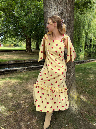 Model wearing the Mila Dress outdoors – strawberry print cotton sundress styled for a summer day, made to order in the UK