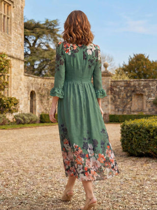 Woman in a green floral dress walking in a garden with a castle-like building in the background