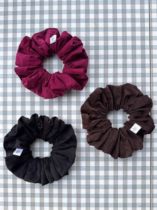 Three scrunchies in black, red, and brown on a checkered background