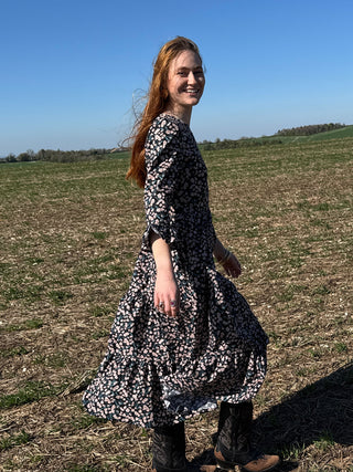 Woman wearing The Well Worn Felicity Dress in floral print, ethically made in the UK, styled with cowboy boots in a spring field.