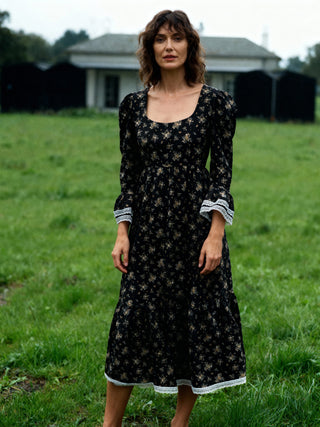 Woman wearing a black floral dress standing in a grassy field.
