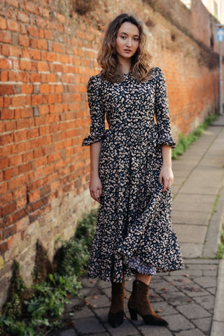 Woman in a floral dress standing against a brick wall.