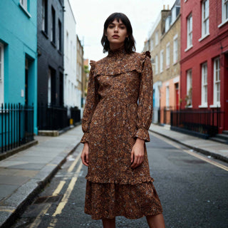 Woman in a brown floral dress standing on a street with colorful buildings.