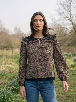 Woman wearing a floral blouse with black lace details outdoors.