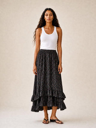 Woman wearing a white tank top and black patterned skirt on a beige background