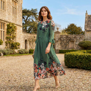 Woman in a green floral dress standing in front of a historic building.