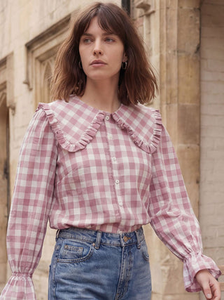 Woman wearing a pink and white checkered blouse with ruffled details in front of a stone building.