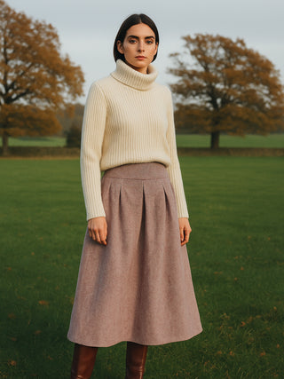 Woman wearing a cream sweater and burgundy skirt standing in a field with trees in the background